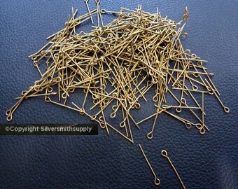 Può includere: Un grande mucchio di spilli per la testa dorati con un anello in cima. Gli spilli sono sparsi su una superficie blu scuro.