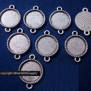 May include: Ten silver-toned round metal pendant trays with a decorative edge. Each tray has three jump rings for attaching to jewelry.