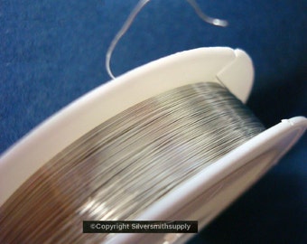 May include: A spool of silver wire on a white plastic bobbin. The wire is wound tightly and is ready to be used for jewelry making or other crafts.