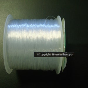 May include: A spool of clear elastic cord, wound around a white plastic bobbin. The cord is used for jewelry making and other crafts.