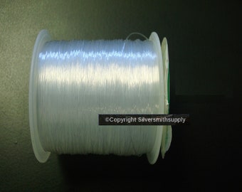 May include: A spool of clear elastic cord, wound around a white plastic bobbin. The cord is used for jewellery making and other crafts.