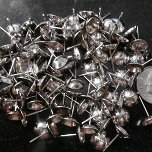 May include: A pile of silver-toned metal nail heads with a domed top. The nail heads are about the size of a ten pence piece.