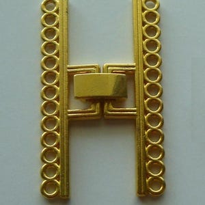 May include: A gold-colored metal component in the shape of the letter "H". The vertical bars feature a series of connected circles along one edge. The horizontal bar is a rectangular shape. The text "Copyright Artistrywithbeads.shop" is at the bottom.