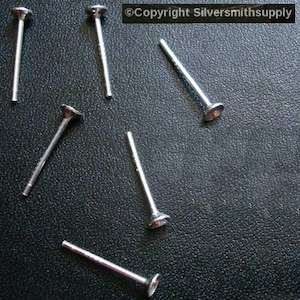 May include: Six silver earring posts with flat round tops. The posts are lying on a textured grey surface. ©Copyright Silversmithsupply