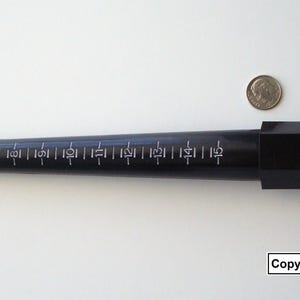 May include: A black ring sizer tool with white measurement markings. The tool is tapered and has a small metal loop at the end. A coin is next to the tool for size comparison. The text "Copyright Artistrywithbeads.shop" is in the bottom right corner.