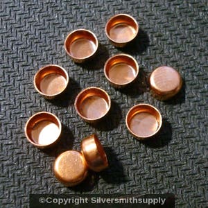 May include: Ten copper-colored metal caps, possibly for jewelry making or other crafts. The caps are round and have a slightly domed shape.