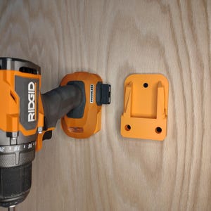 May include: An orange and black Ridgid brand drill with a matching orange battery and wall mount. The drill is partially visible, with the battery and mount attached to a wooden surface.