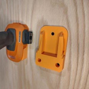 May include: An orange and black cordless drill and a matching orange wall mount. The drill has the word "BRUSHLESS" printed on it. The wall mount has two holes for mounting and a slot to hold the drill.