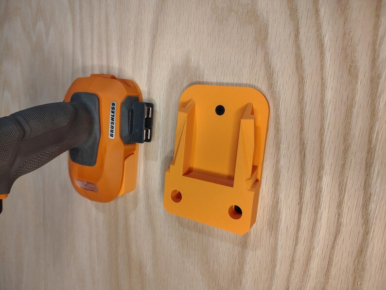 May include: An orange and black cordless drill and a matching orange wall mount. The drill has the word "BRUSHLESS" printed on it. The wall mount has two holes for mounting and a slot to hold the drill.