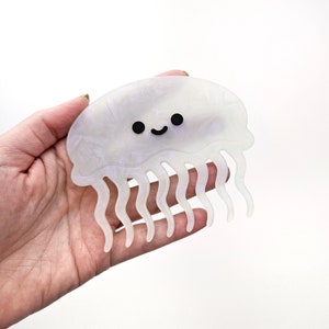 May include: A white iridescent plastic hair clip shaped like a smiling jellyfish with black eyes.