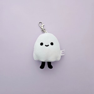 May include: White plush ghost keychain with black eyes and a smiling mouth. The ghost has small black legs and a silver keychain loop. The tag on the ghost reads "This Thing".