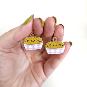May include: Gold dangle earrings with a pink and white checkered basket filled with three smiling yellow chicken nuggets.
