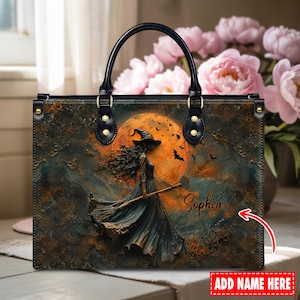 May include: A rectangular handbag with black handles and gold hardware. The front features a dark, textured scene of a witch in a long dress holding a broomstick against a large orange moon with flying bats. The name Sophia is printed in script.