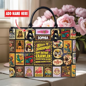Könnte beinhalten: Schwarze Lederhandtasche mit bunten, stempelförmigen Designs, die Cartoon-Tiere und Text zeigen. Die Tasche hat einen schwarzen Griff und den Namen "SOPHIA". Ein einzigartiges Accessoire.