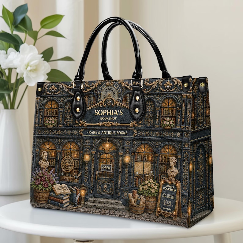 Vintage bookstore handbag shown on a clean indoor table, featuring a detailed antique bookshop design with golden accents, warm window lights, flower baskets, books, statues, black handles, and structured side panels. A charming personalized book lover bag for readers, librarians, teachers, writers, book collectors, and fans of classic literary style.