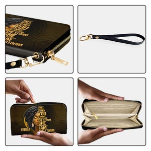 Puede incluir: Cartera negra con cremallera dorada y correa de mu&ntilde;eca. La cartera presenta un retrato de una mujer y el texto "THEY TRIED TO HER YOU CANNOT WITHSTAND THE STORM SHE I AM THE STORM".