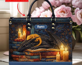 Puede incluir: Bolso tote con temática de fantasía. El bolso presenta un dragón negro y un dragón dorado sobre una pila de libros, con velas encendidas. El bolso tiene un estampado floral azul y un asa negra. El nombre "Sophia" está en el bolso.