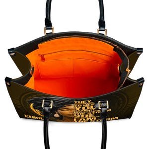 Open view of custom empowerment handbag showing orange interior lining, multiple pockets, and zippered compartments. Faux leather tote with “I Am The Storm” quote and Black woman art. Personalized with name for unique style. Functional and fashionable bag for everyday use, work, or travel. Ideal personalized gift for women, Christmas or birthday.