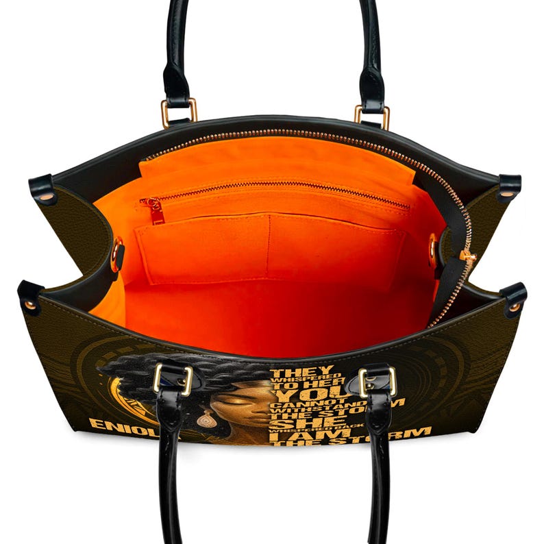 Open view of custom empowerment handbag showing orange interior lining, multiple pockets, and zippered compartments. Faux leather tote with “I Am The Storm” quote and Black woman art. Personalized with name for unique style. Functional and fashionable bag for everyday use, work, or travel. Ideal personalized gift for women, Christmas or birthday.
