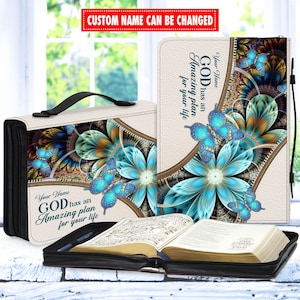 May include: A white leather Bible cover with a zipper closure. The cover features a colorful floral design with blue butterflies and the text "Your Name GOD has an Amazing plan for your life".