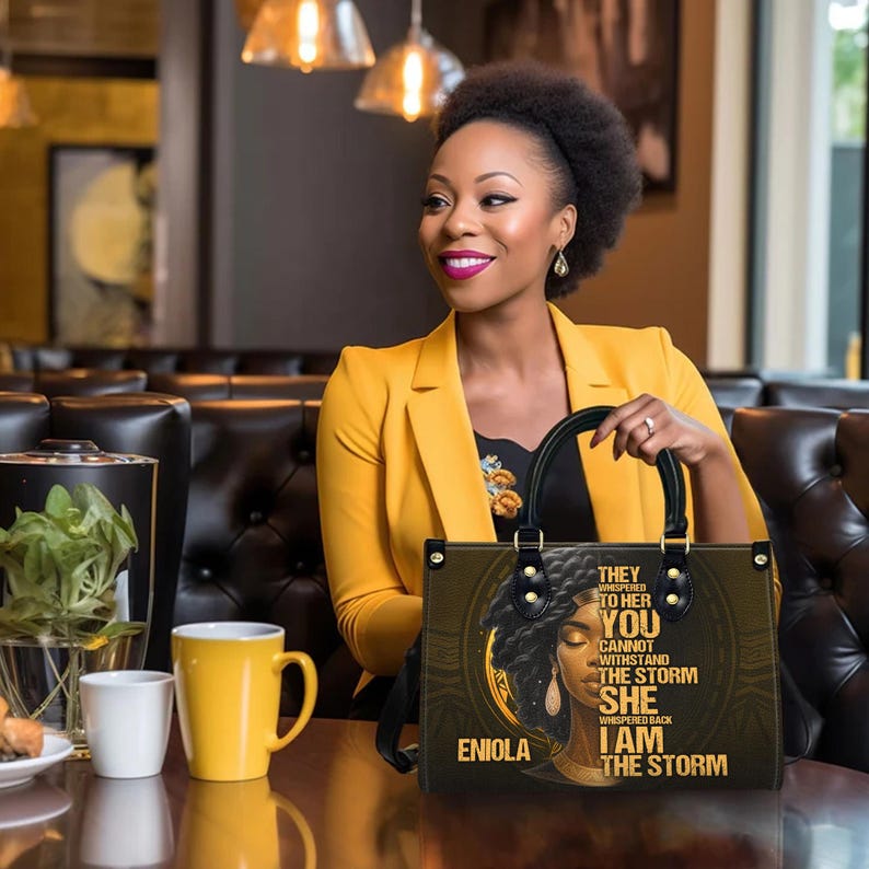 Beautiful personalized leather tote bag shown in use by stylish woman. Black girl magic handbag with inspiring quote “I Am The Storm,” custom name option, durable PU leather with twill finish. Perfect everyday purse or empowerment gift for Black women, mom, or grandma. Great for birthdays, Mother’s Day, or Christmas gift ideas for her.
