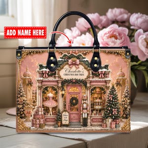 May include: A rectangular handbag with black handles and gold hardware featuring a printed illustration of a pink Christmas boutique storefront. The text reads Charlotte's CHRISTMAS BOUTIQUE, Ballet Dreams, Music & Magic, and Believe in the Magic.