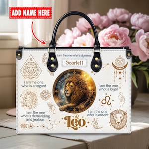 May include: White tote bag with black handles and gold hardware. The bag features a lion graphic with the text "Leo" and "Scarlett". Additional text includes "I am the one who is dynamic", "I am the one who is arrogant", "I am the one who is loyal", "I am the one who is demanding and jealous", and "I am the one who is ardent".