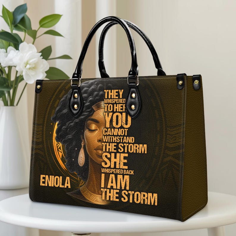 Close-up of custom faux leather handbag with bold Black woman portrait and motivational quote “I Am The Storm.” Personalized with name for a unique gift. PU and twill leather finish with elegant black handles. Ideal tote bag for everyday wear, work, or travel. Great personalized Christmas gift, empowerment present, or stylish accessory for Black women.