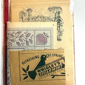 May include: A collection of vintage ephemera, including cross-stitch patterns and a Wrigley's Spearmint gum advertisement. The cross-stitch design features a floral motif in pink and purple. The gum ad has a black bird graphic.