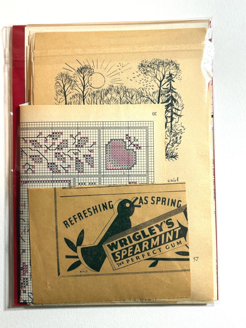 May include: A collection of vintage ephemera, including cross-stitch patterns and a Wrigley's Spearmint gum advertisement. The cross-stitch design features a floral motif in pink and purple. The gum ad has a black bird graphic.