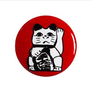 May include: A red and white lucky cat figurine with a raised paw. The cat is sitting on a red circle.