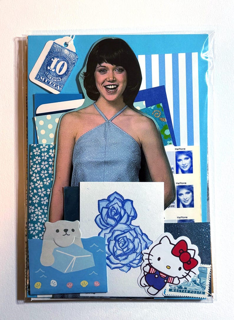 Mystery ephemera pack in Blue, showing vintage texts, picture of woman in blue halter tank top from a sewing pattern, decorative papers, art print with blue roses, cancelled postage stamp, glitter paper, and stickers.