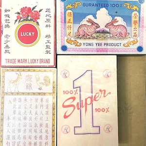 May include: A collection of vintage boxes with various designs and text. One box features the word "LUCKY" with floral accents. Another displays two rabbits with the text "YONG YEE PRODUCT." A third box has a large number "1" with the word "Super." The boxes are in various colors.