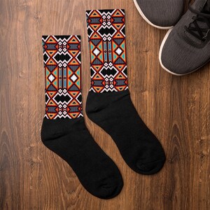 May include: A pair of black socks with a geometric pattern in shades of orange, red, white, blue, and gray. The pattern is reminiscent of Native American art.