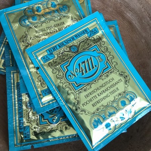Può includere: Un pacchetto di bustine in lamina blu e oro con il testo "Echt Kölnisch Wasser Original Eau de Cologne No. 4711" e "Refreshing Tissue Pochette rafraîchissante" stampato su di esse.