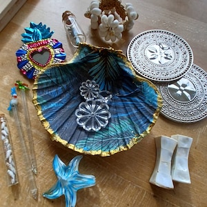 May include: A collection of decorative items including a blue and gold seashell, clear glass starfish, silver coasters, and a heart-shaped mirror. Other items include a seashell bracelet, glass vials, and clear flower-shaped ornaments.