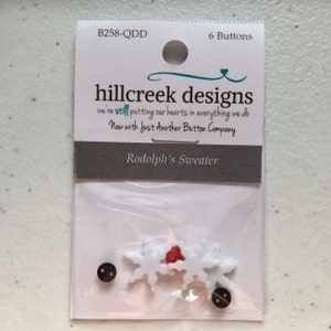 May include: A package of six white snowflake buttons with red accents. The package is labeled "hillcreek designs" and "Rodolph's Sweater".