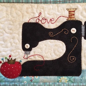 May include: A black sewing machine with red thread and the word "love" stitched above it. A red and white pincushion with green and blue pins is in the foreground.