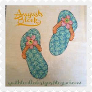 May include: A pair of blue and green flip-flops with orange straps and pink flowers. The flip-flops have a button in the centre of each flower. The text "Augusts Block" is written in orange at the top of the image.