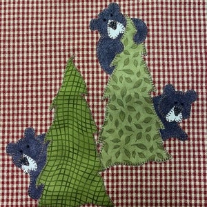 May include: Three black bears are hiding in green trees with brown and white checkered fabric in the background.