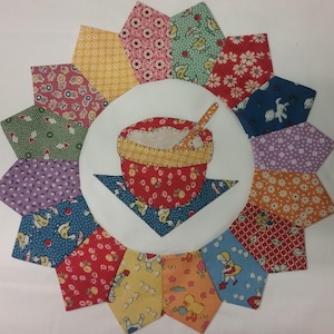 May include: A colorful patchwork quilt block with a central image of a red bowl with a yellow rim and a wooden spoon. The bowl is filled with white fabric and the spoon is resting on the top of the bowl. The quilt block is made up of 16 individual pieces of fabric, each with a different pattern. The fabric patterns include floral prints, geometric patterns, and animal prints.