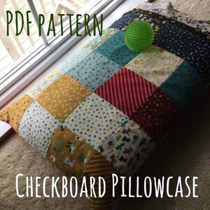 May include: PDF pattern for a checkered pillowcase featuring a range of dog-themed fabrics in shades of blue, red, yellow, and brown. The pillowcase is displayed on a carpet with a green spiky ball toy.
