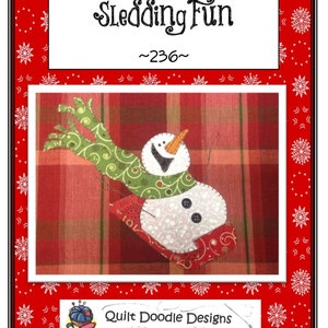 May include: A red and green plaid fabric with a snowman on a sled. The snowman is white with black eyes and a carrot nose. The text "Sledding Fun ~236~" is above the image and "Quilt Doodle Designs" is below the image.