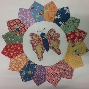 May include: A colourful patchwork quilt block featuring a central butterfly applique. The butterfly is blue, yellow and red with a floral pattern. The quilt block is made from various fabrics with floral and geometric patterns in shades of red, green, blue, yellow and purple.