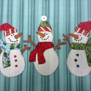 Puede incluir: Tres adornos de muñeco de nieve hechos de tela con sombreros y bufandas de diferentes colores. El muñeco de nieve de la izquierda tiene un sombrero a rayas rojo y blanco y una bufanda azul y verde. El muñeco de nieve del medio tiene un sombrero verde con una bufanda roja. El muñeco de nieve de la derecha tiene un sombrero rojo con una bufanda verde.