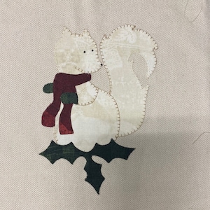 May include: A white felt squirrel with a red and green scarf sitting on a green felt holly leaf.
