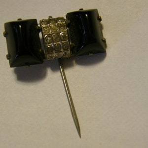 Puede incluir: Un broche de lazo negro y plateado con un alfiler. El lazo est&aacute; hecho de tres piezas de vidrio negro con una banda plateada de diamantes de imitaci&oacute;n en el centro.