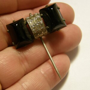 Puede incluir: Un broche vintage negro y plateado con dos piedras rectangulares negras y una banda plateada de diamantes de imitaci&oacute;n. El broche tiene un largo cierre de aguja plateado.