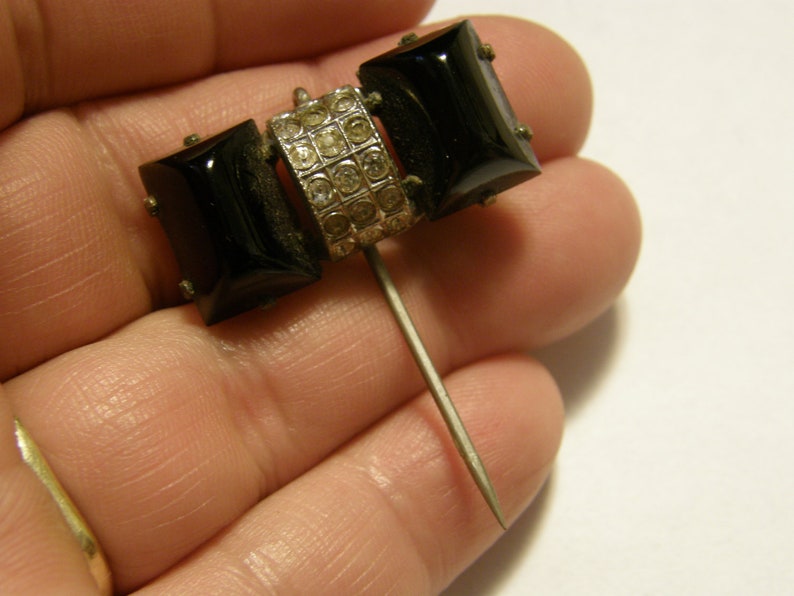 Puede incluir: Un broche vintage negro y plateado con dos piedras rectangulares negras y una banda plateada de diamantes de imitaci&oacute;n. El broche tiene un largo cierre de aguja plateado.