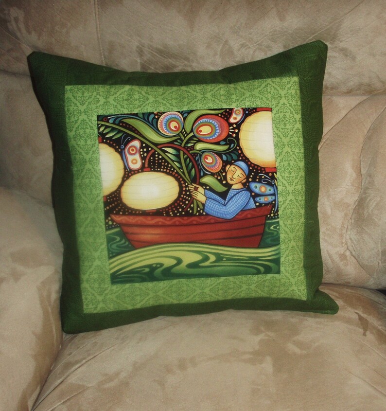 May include: A green pillow with a colorful illustration of a person in a boat surrounded by flowers and lights. The pillow has a green border with a decorative pattern.